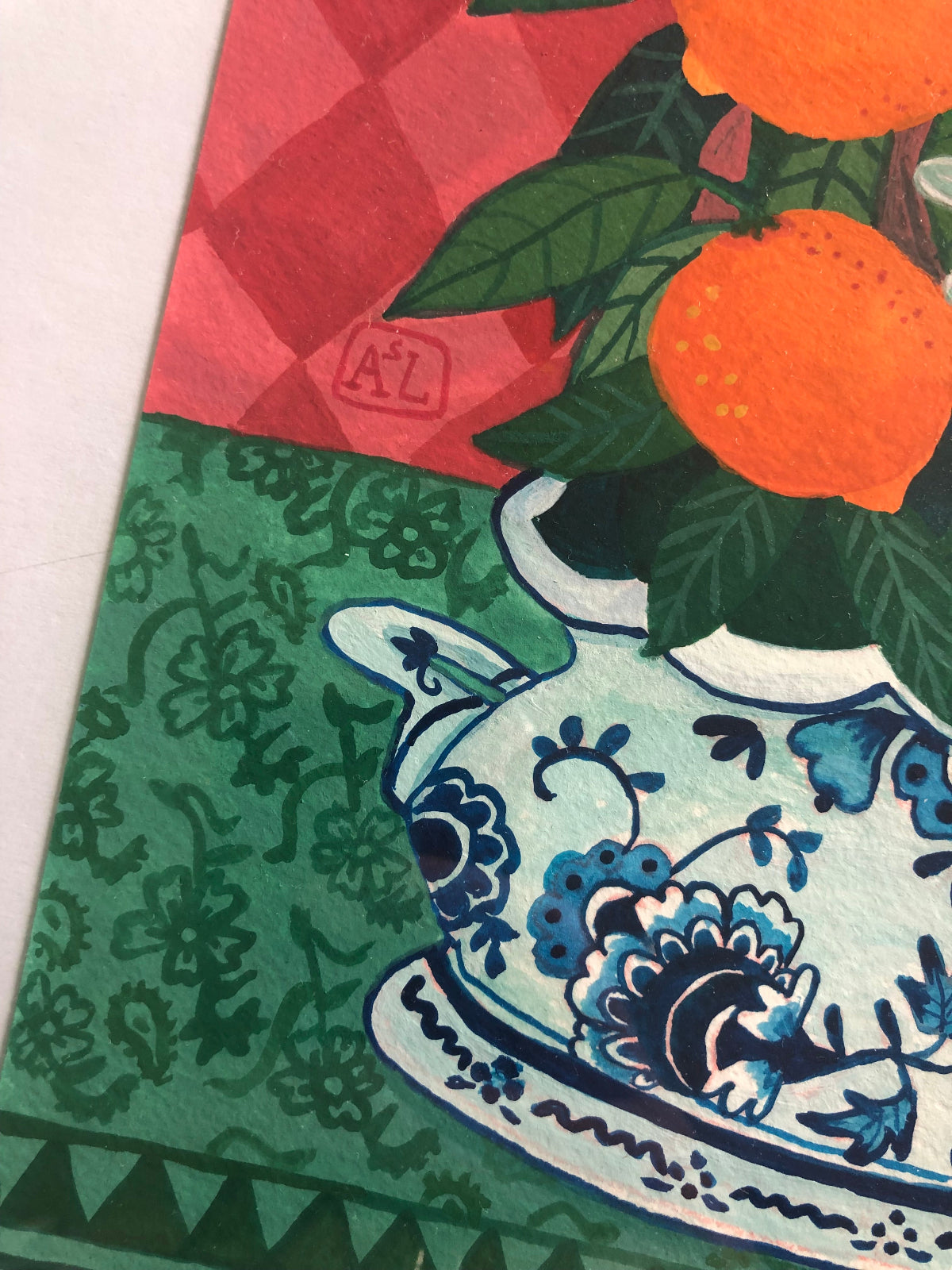 handgeschilderd stilleven schilderij met een sinaasappel boompje vol sinaasappels en sinaasappel bloesem in Blauw witte delfts blauwe schaal. De achtergrond van dit hippe schilderij heeft roze ruiten. Een handgemaakt figuratief schilderij in knalkleuren met knalroze, knaloranje en felroze.