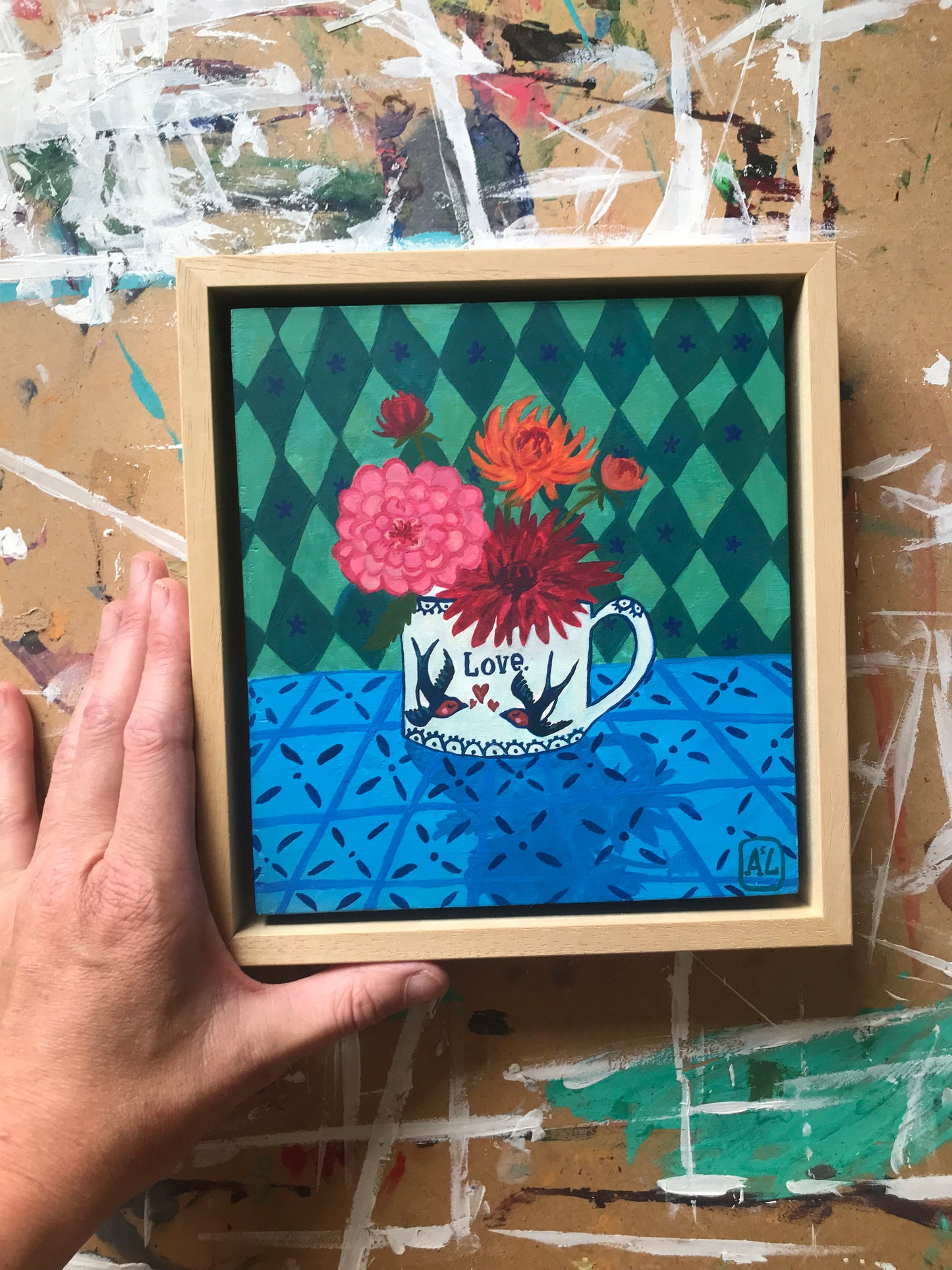 Handgeschilderd schilderij met een Vrolijk kleurrijk dahlia stilleven. Op dit gezellige hippe schilderij staat een theekopje met bloemen uit de tuin en op het theekopje staan twee vogeltjes, namelijk zwaluwen. Ook staat er de tekst liefde op. Dit kleine handgemaakte schilderij is ook geschikt als kado voor huwelijk, liefde of valentijnsdag. Dit schilderijtje is geschilderd en is een eigentijds kunstwerkje in felle kleuren als fuchsia roze, oranje rood en emerald groene met mintgroen wiebertjes patroon.