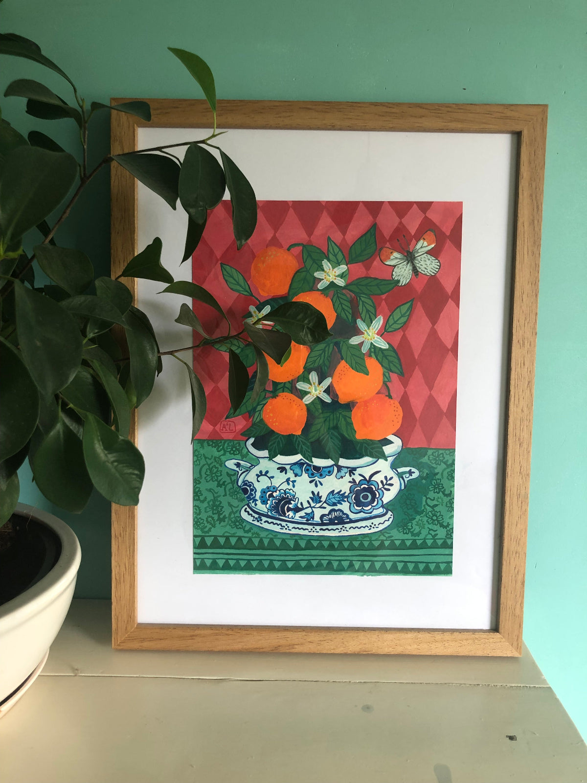 handgeschilderd stilleven schilderij met een sinaasappel boompje vol sinaasappels en sinaasappel bloesem in Blauw witte delfts blauwe schaal. De achtergrond van dit hippe schilderij heeft roze ruiten. Een handgemaakt figuratief schilderij in knalkleuren met knalroze, knaloranje en felroze.