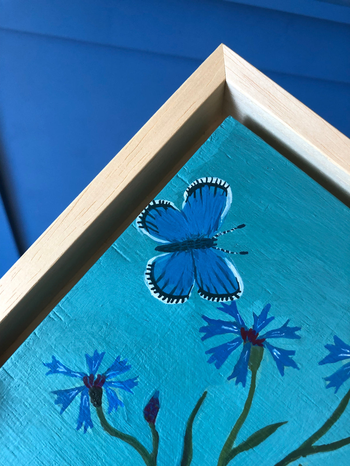 kleurrijk handgeschilderd korenbloem stilleven in blauwe tinten. De korenbloempjes staat in een burgenland  theekopje van villeroy en boch. Op dit handgemaakte schilderij staan ook twee blauwe vlindertjes. Dat zijn icarus blauwtjes.