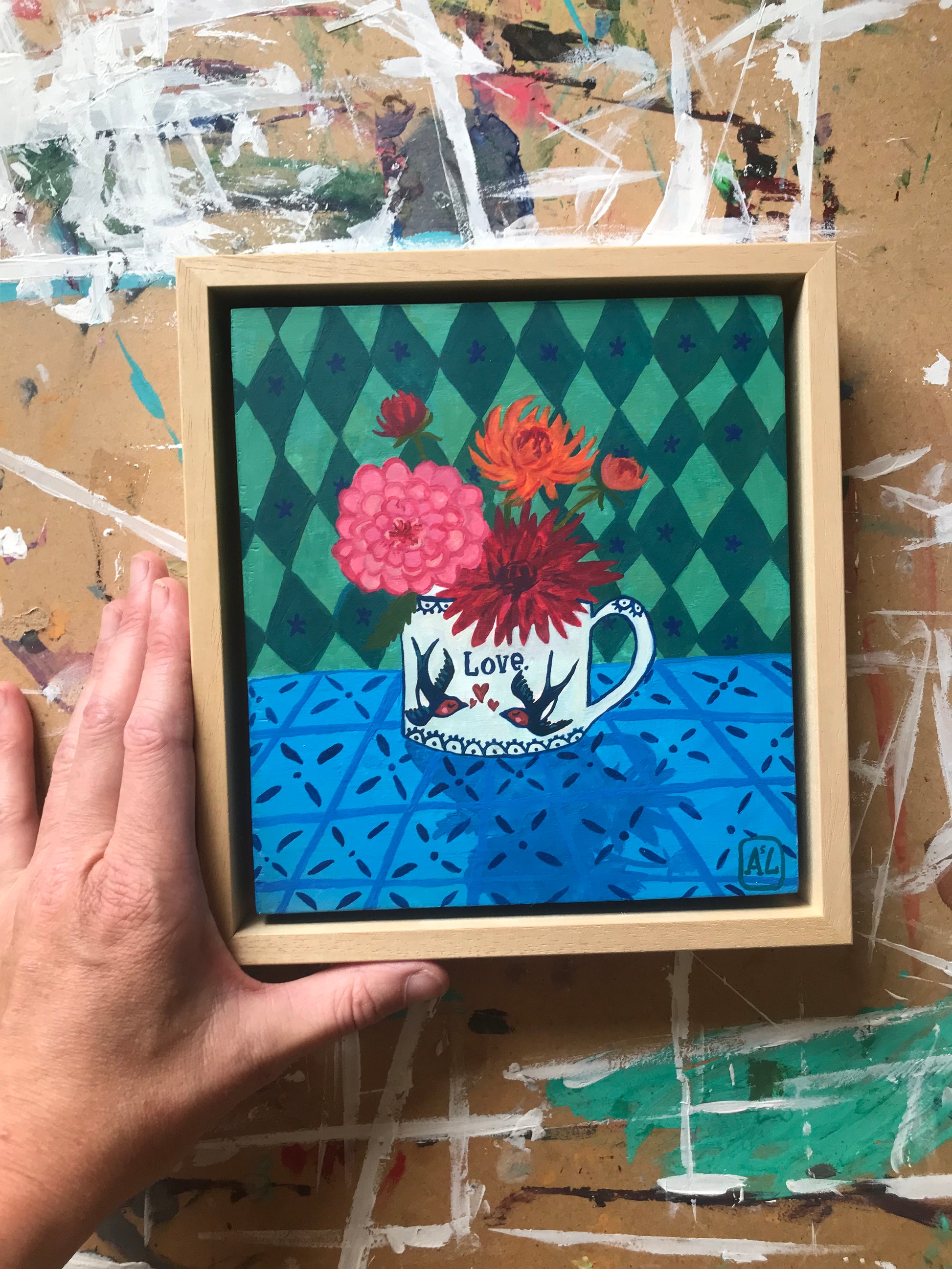 Handgeschilderd schilderij met een Vrolijk kleurrijk dahlia stilleven. Op dit gezellige hippe schilderij staat een theekopje met bloemen uit de tuin en op het theekopje staan twee vogeltjes, namelijk zwaluwen. Ook staat er de tekst liefde op. Dit kleine handgemaakte schilderij is ook geschikt als kado voor huwelijk, liefde of valentijnsdag. Dit schilderijtje is geschilderd en is een eigentijds kunstwerkje in felle kleuren als fuchsia roze, oranje rood en emerald groene met mintgroen wiebertjes patroon. 