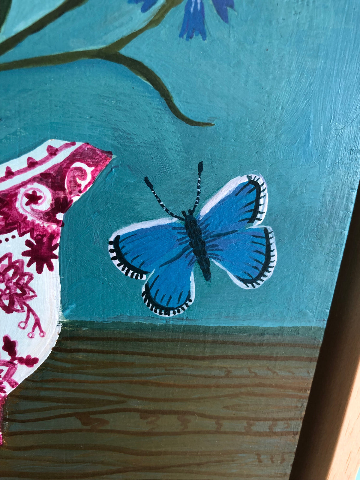 kleurrijk handgeschilderd korenbloem stilleven in blauwe tinten. De korenbloempjes staat in een burgenland  theekopje van villeroy en boch. Op dit handgemaakte schilderij staan ook twee blauwe vlindertjes. Dat zijn icarus blauwtjes.