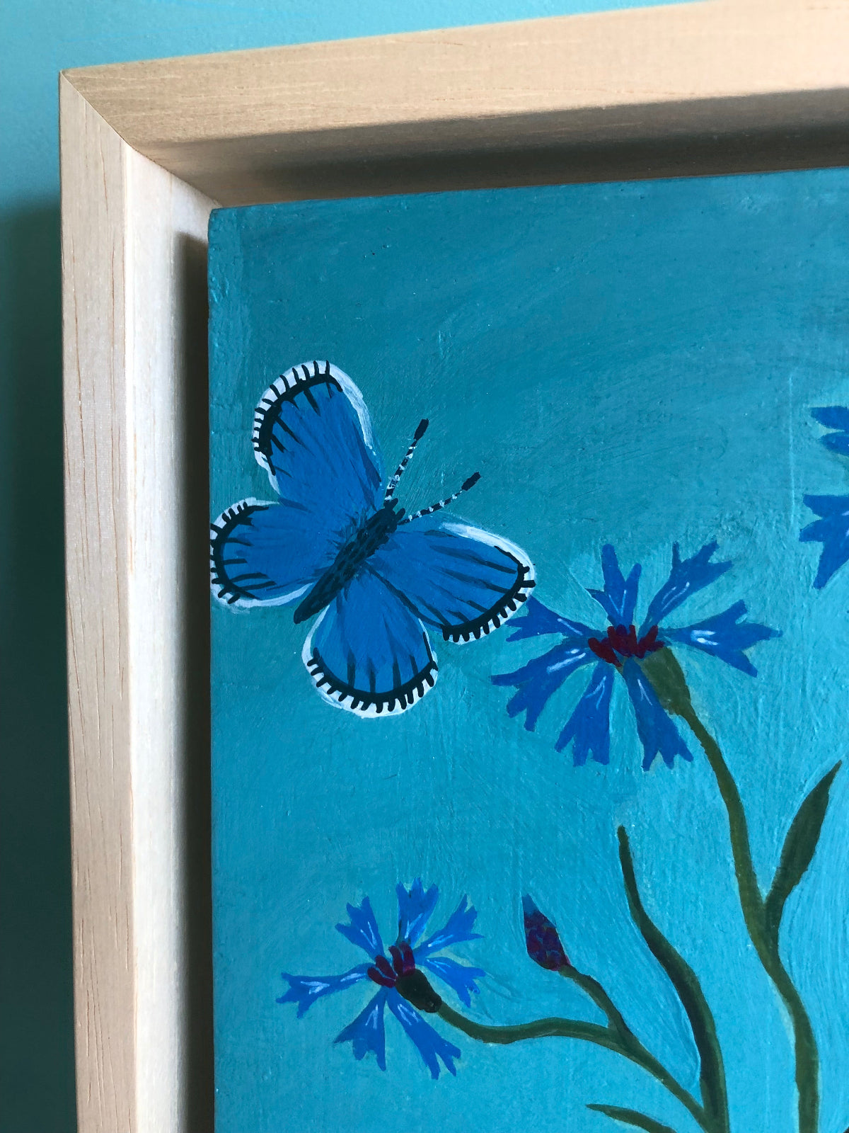 kleurrijk handgeschilderd korenbloem stilleven in blauwe tinten. De korenbloempjes staat in een burgenland  theekopje van villeroy en boch. Op dit handgemaakte schilderij staan ook twee blauwe vlindertjes. Dat zijn icarus blauwtjes.