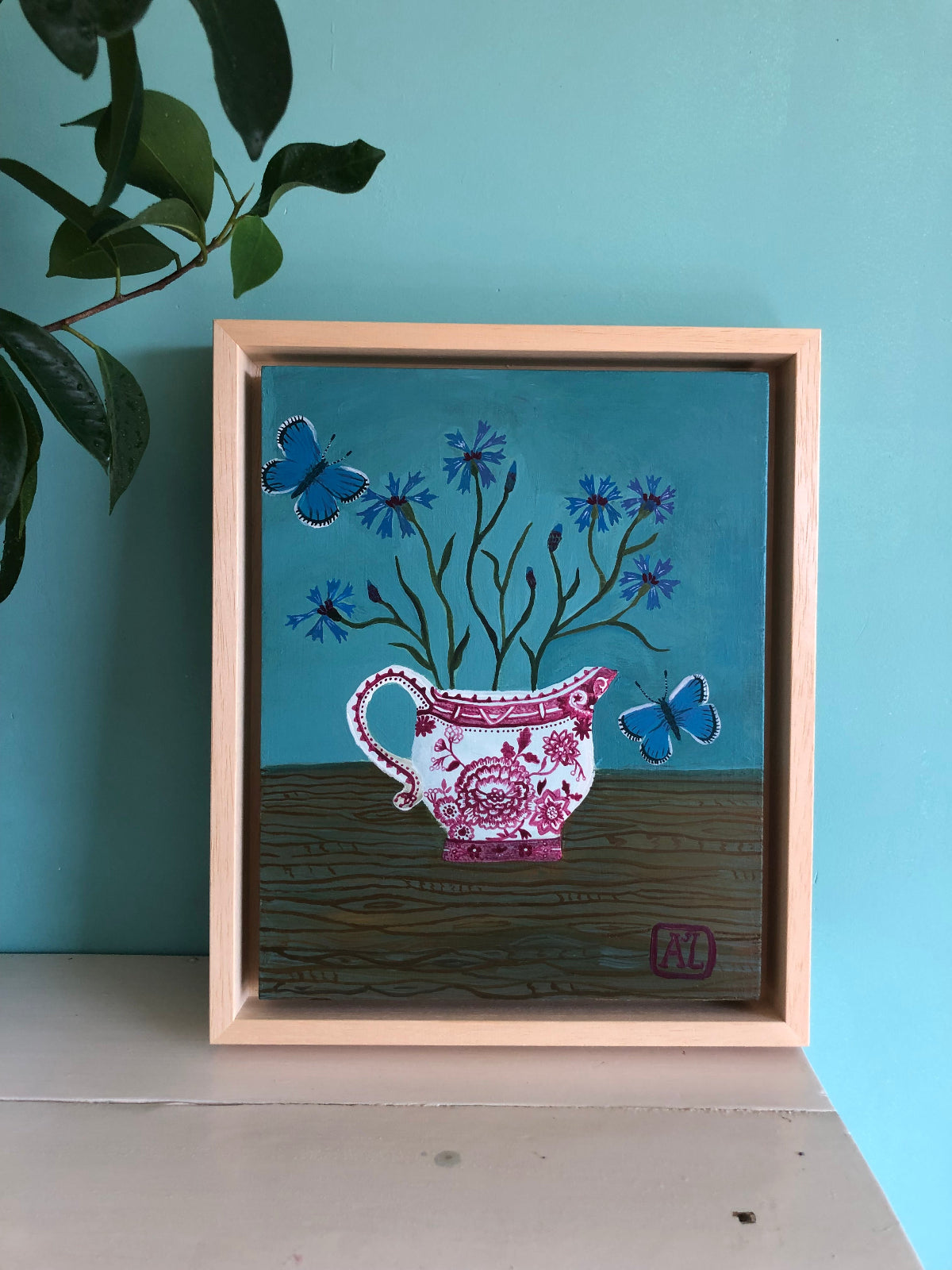 kleurrijk handgeschilderd korenbloem stilleven in blauwe tinten. De korenbloempjes staat in een burgenland  theekopje van villeroy en boch. Op dit handgemaakte schilderij staan ook twee blauwe vlindertjes. Dat zijn icarus blauwtjes.